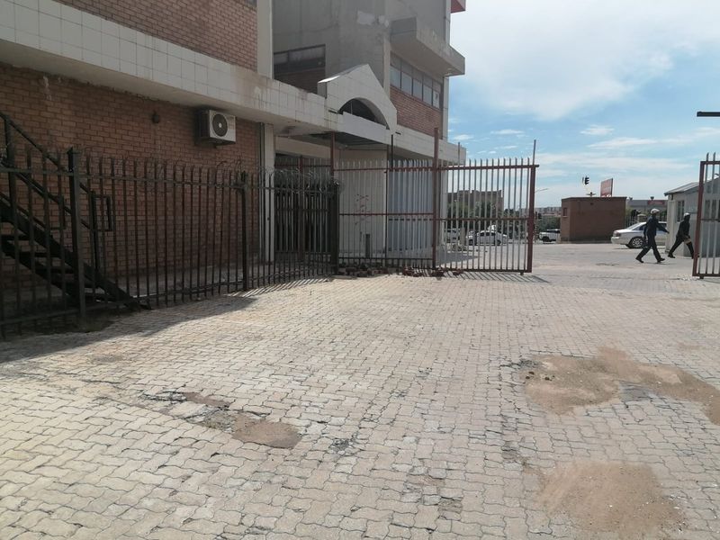 Front exterior view of a commercial building featuring brick facade, metal security fencing, and a paved driveway area showing signs of wear.