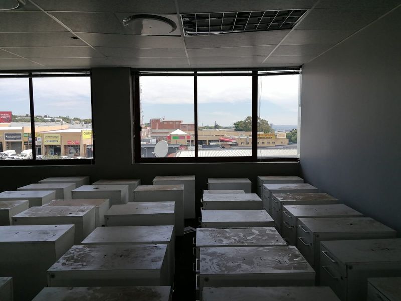 An empty commercial office space featuring large windows with street views, a suspended ceiling, and recessed lighting, suitable for various business configurations.