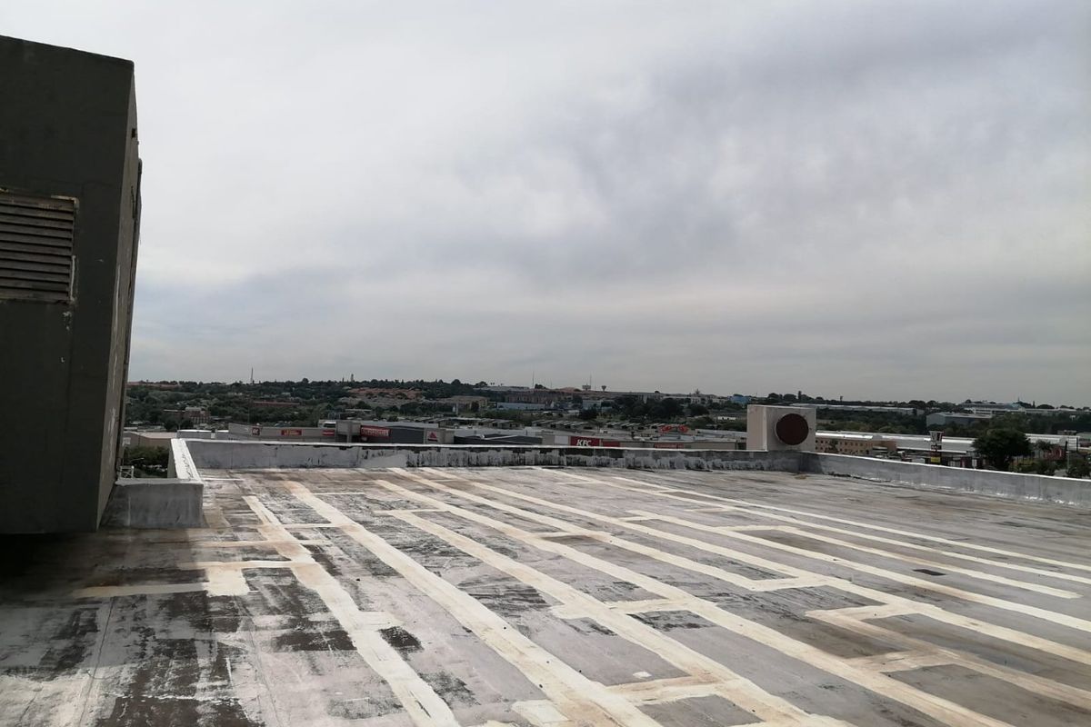 A view of a flat commercial rooftop with a parapet wall and ventilation infrastructure, showing signs of significant weathering and wear.