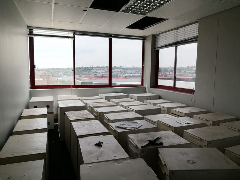A commercial office space featuring large windows with city views, suspended ceiling tiles, and multiple storage units.