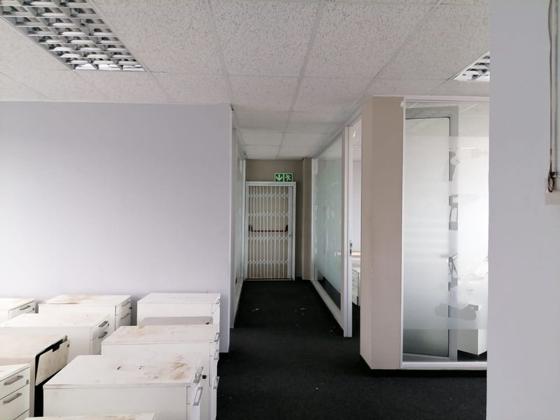 Commercial office space featuring glass partitions, suspended ceilings with recessed lighting, and a secure entrance gate, providing a functional layout for professional use.