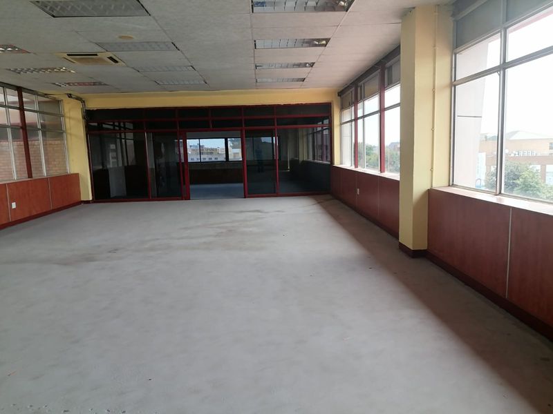 An empty, open-plan commercial office space featuring large windows, wood veneer wall paneling, and a suspended ceiling with recessed lighting.