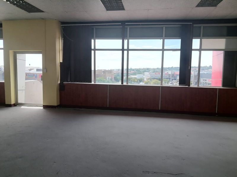An empty commercial office space featuring large windows with city views, wood paneling, and a suspended ceiling, suitable for a modern workspace renovation.