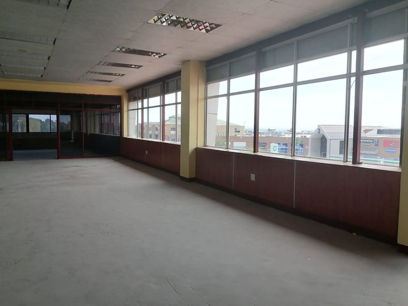 Spacious, vacant commercial office area featuring large windows, wood paneling, and recessed lighting, offering a blank canvas for professional workspace customization.