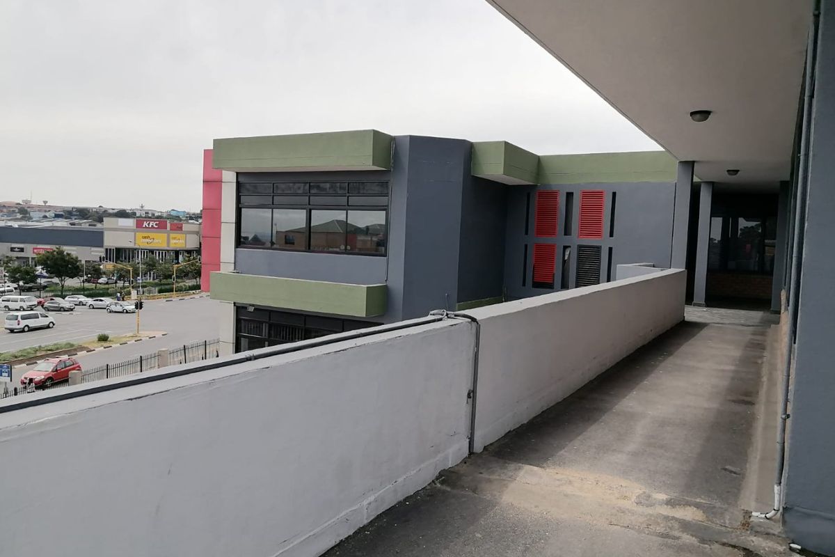 An elevated outdoor walkway or balcony area featuring a concrete balustrade, overlooking a commercial parking area and surrounding urban infrastructure.