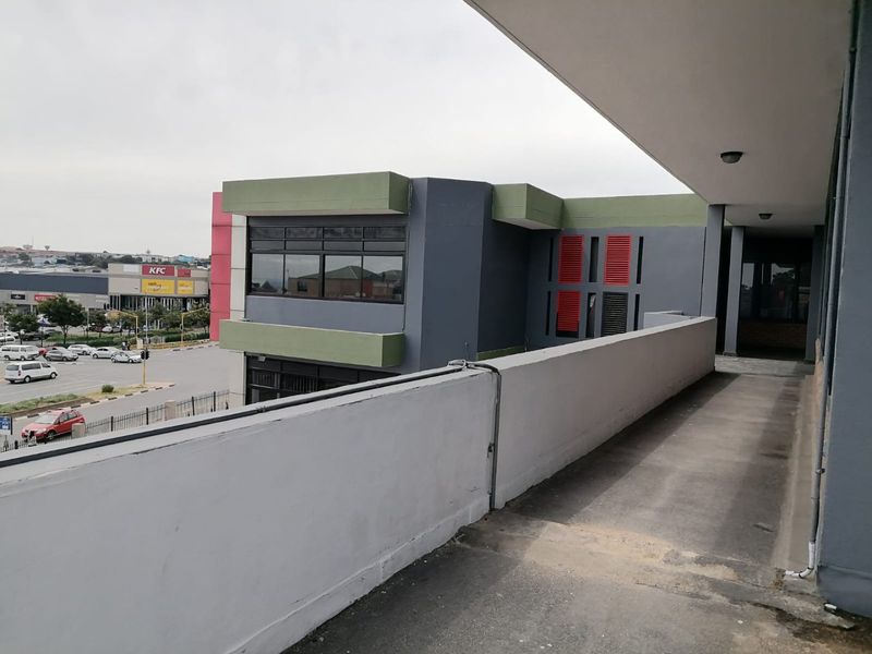 An elevated outdoor walkway or balcony area featuring a concrete balustrade, overlooking a commercial parking area and surrounding urban infrastructure.