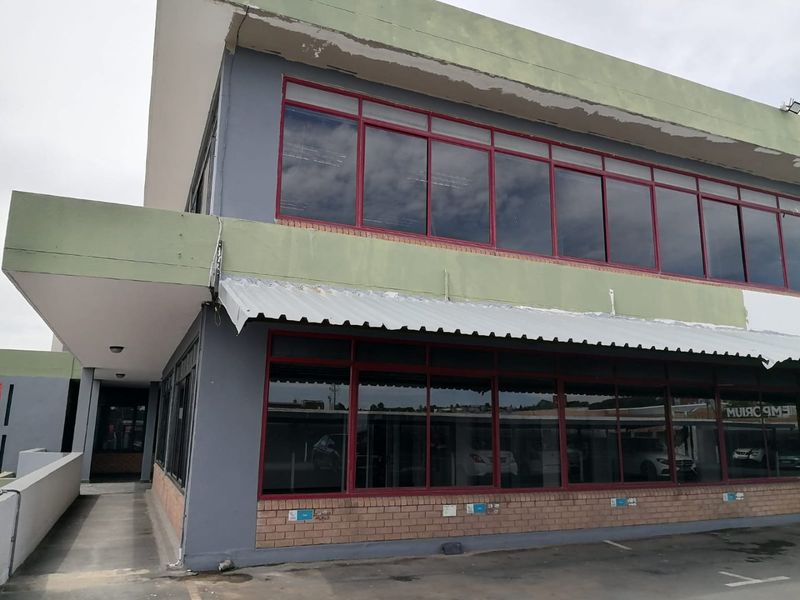 Exterior view of a two-story commercial building featuring large aluminium-framed windows, a corrugated metal awning, and a brick facade base.