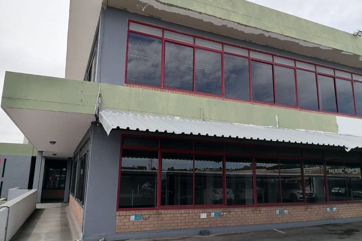 Exterior view of a two-story commercial building featuring large aluminium-framed windows, a corrugated metal awning, and a brick facade base.