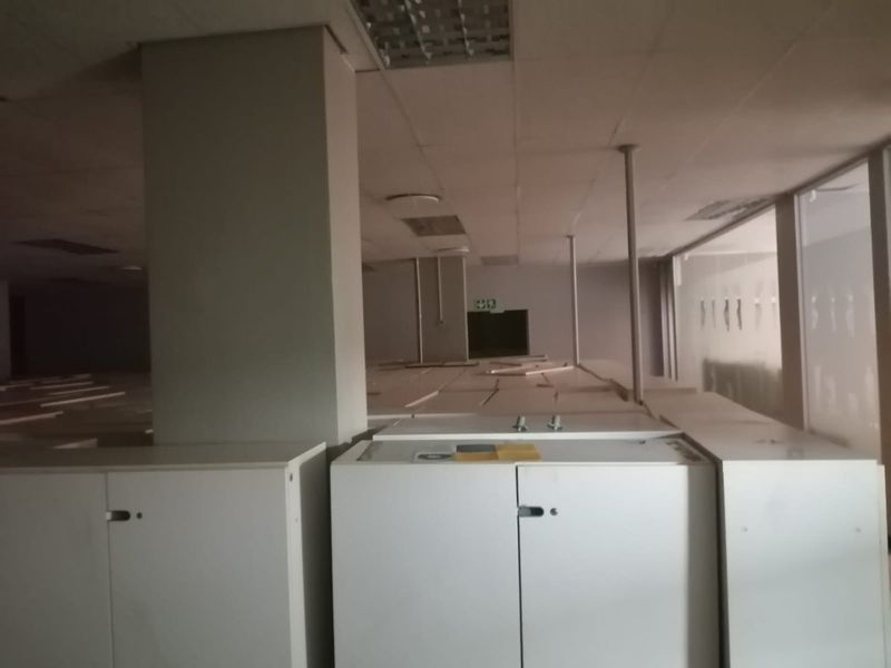 An empty commercial office space featuring a suspended ceiling, support columns, and built-in storage cabinetry, requiring cosmetic updates.