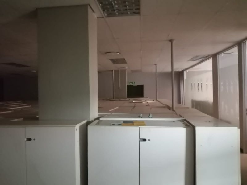 An empty commercial office space featuring a suspended ceiling, built-in cabinetry, and support columns, currently in need of refurbishment.