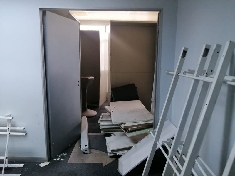 A utility or storage area showing signs of wear, featuring a suspended ceiling and internal access door, currently containing construction debris.