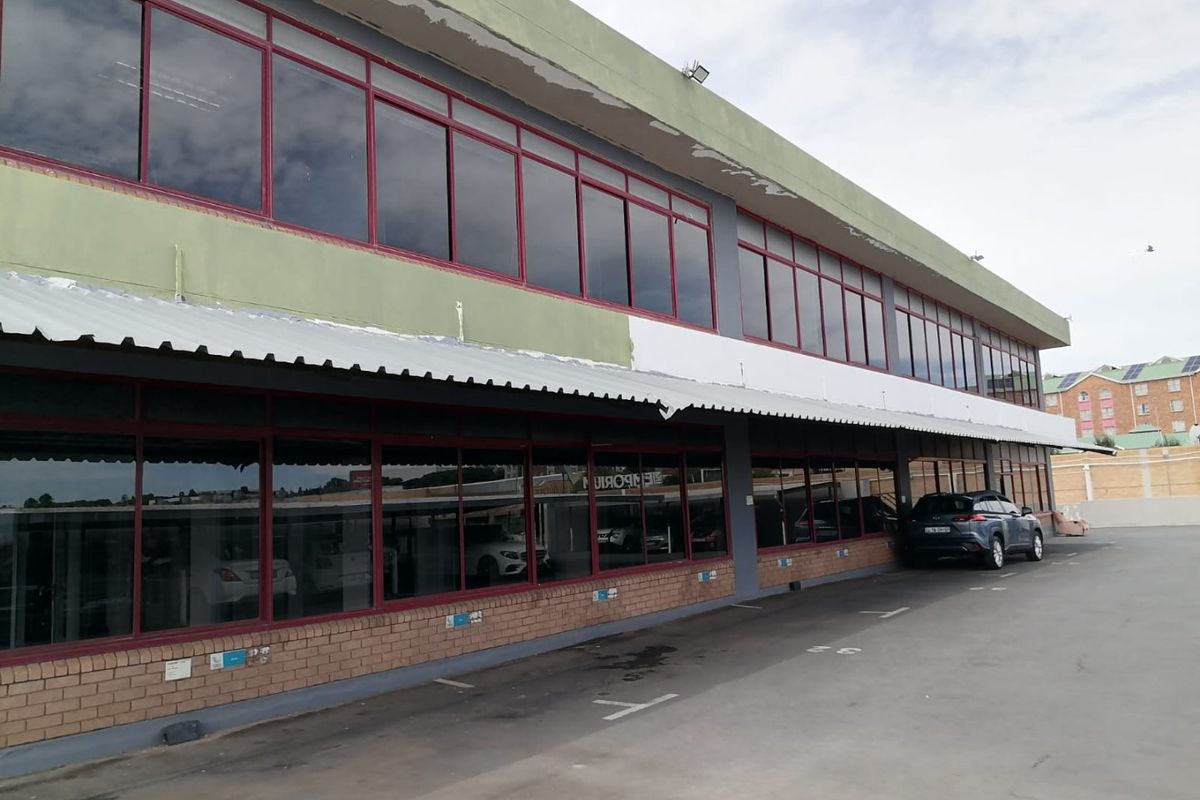 Exterior view of a commercial building featuring a brick base, extensive aluminium-framed windows, and a metal awning over a paved parking area.