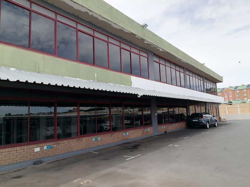 Exterior view of a commercial building featuring a brick base, extensive aluminium-framed windows, and a metal awning over a paved parking area.