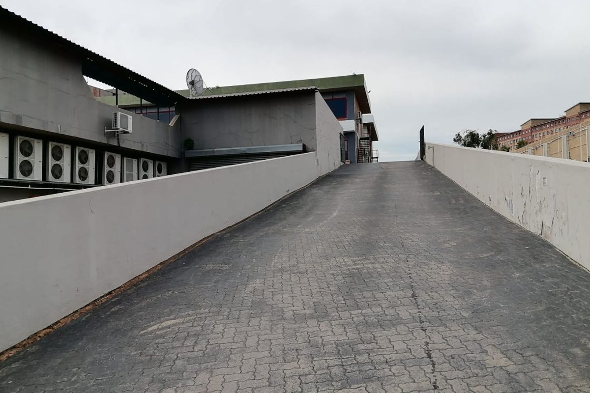 Commercial property exterior featuring a paved access ramp with retaining walls and multiple external air conditioning units mounted on the building facade.