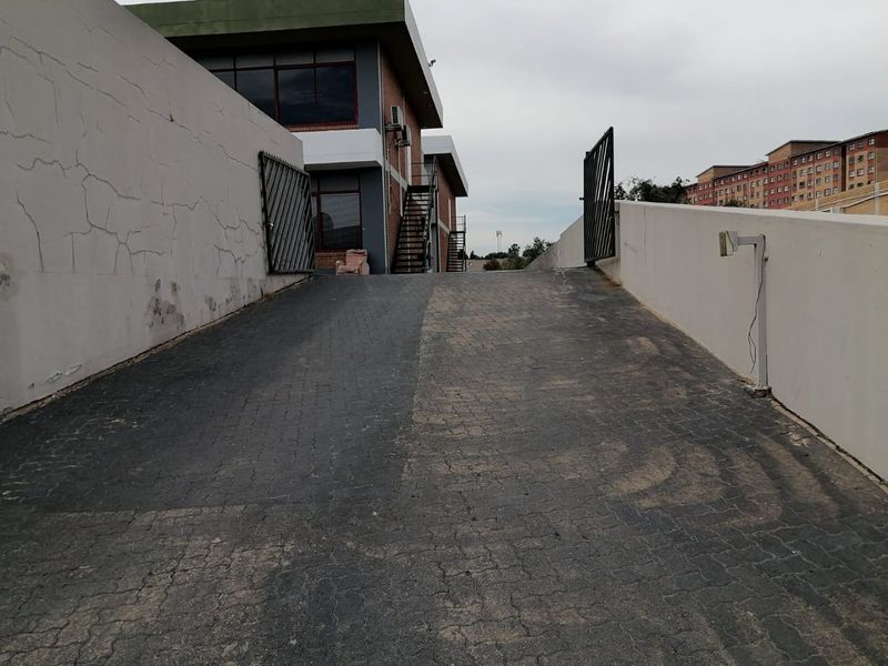 A paved driveway ramp leading to a commercial building entrance, featuring retaining walls, security gates, and external metal staircases.