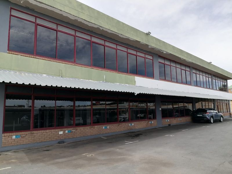 Commercial building exterior featuring a two-story facade with extensive aluminium-framed windows, a protective metal awning, and an adjacent asphalt parking area.