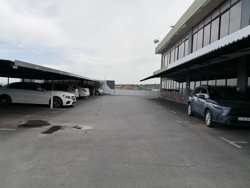 Commercial property exterior featuring a paved parking area with covered bays and a multi-story building with extensive glass frontage.