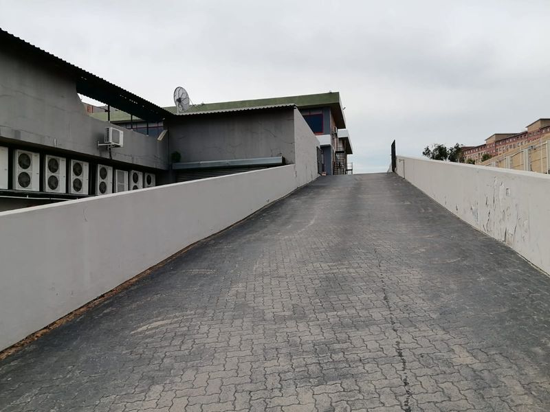 Commercial property exterior featuring a paved access ramp with retaining walls and multiple external air conditioning units mounted on the building facade.