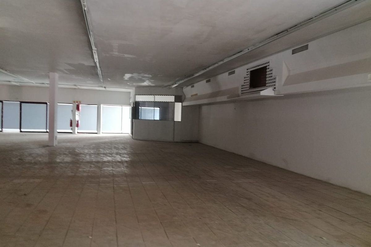 Spacious open-plan commercial interior featuring tiled flooring, a glass-partitioned office area, and suspended ceiling, currently vacant and ready for renovation.