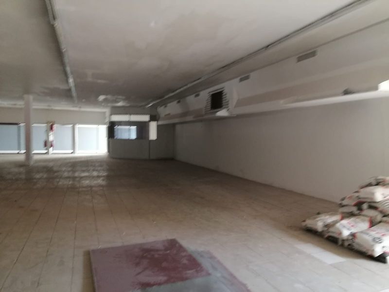 A spacious, vacant commercial open-plan area featuring tiled flooring, large windows, and recessed ceiling lighting, currently in need of cosmetic refurbishment.