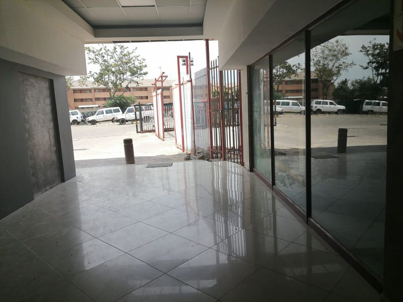 A bright commercial entrance area featuring polished tiled flooring, large glass display windows, and a secure metal gate leading to the exterior parking area.