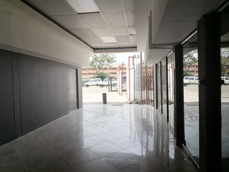 A vacant commercial entry space featuring polished tiled flooring, a suspended ceiling, and large glass panels providing visibility to the exterior parking area.