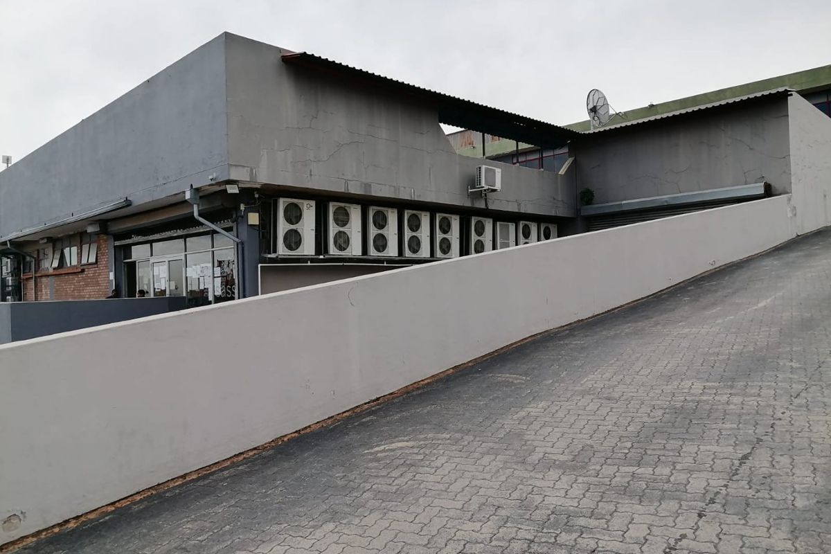 Commercial property exterior featuring a paved access ramp, retaining wall, and multiple external air conditioning units mounted on the building facade.