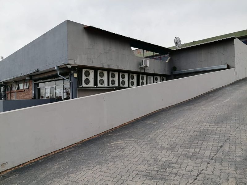 Commercial property exterior featuring a paved access ramp, retaining wall, and multiple external air conditioning units mounted on the building facade.