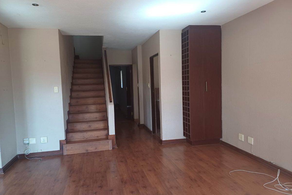An open-plan living area featuring laminate flooring, a wooden staircase, and a built-in wine storage unit, presenting a blank canvas for interior design.