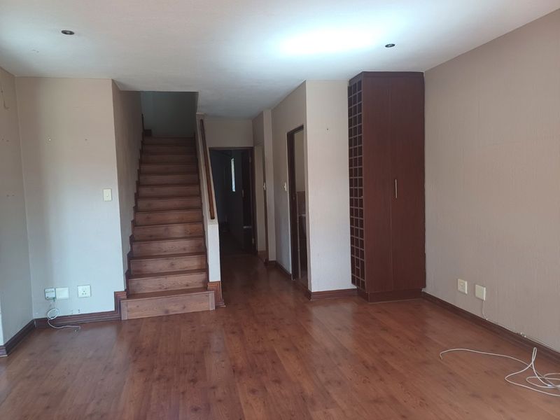 An open-plan living area featuring laminate flooring, a wooden staircase, and a built-in wine storage unit, presenting a blank canvas for interior design.