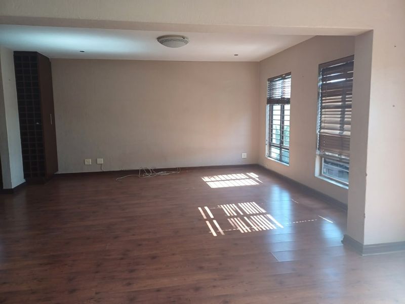Spacious living area featuring warm laminate flooring, built-in wine storage cabinetry, and large windows with fitted venetian blinds.