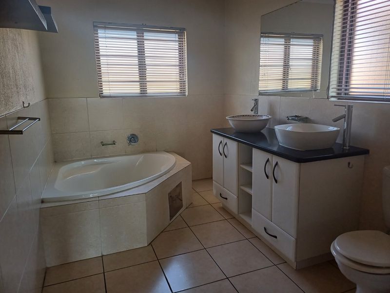A functional bathroom featuring a built-in corner bathtub, a double vanity with vessel sinks, and neutral wall and floor tiling.