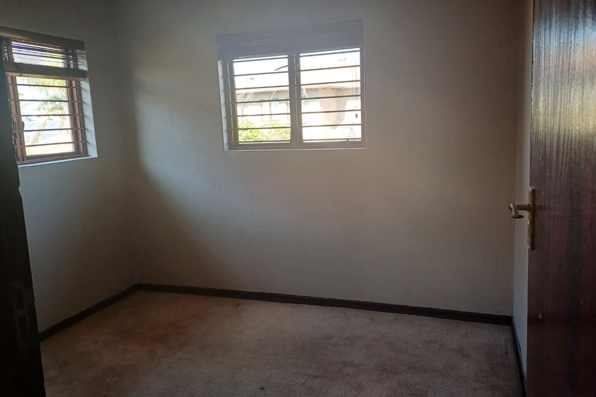 An empty bedroom featuring carpet flooring, security bars on the windows, and a timber door.