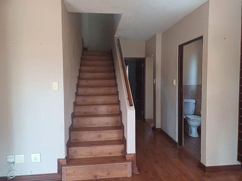 A hallway featuring a wooden staircase with a handrail, hardwood flooring, and access to an adjacent bathroom.