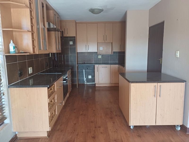 A functional kitchen featuring light wood cabinetry, dark granite countertops, a tiled backsplash, and a mobile kitchen island with matching finishes.