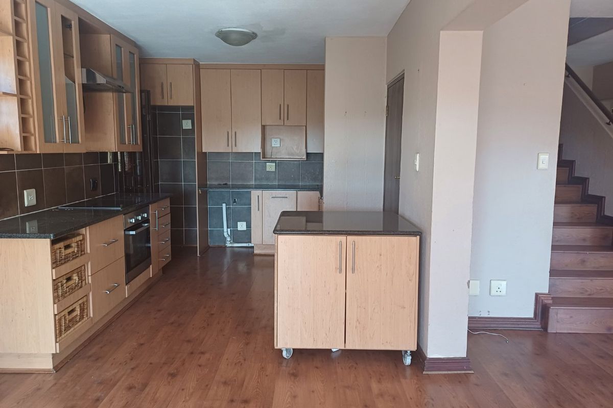 Kitchen featuring light wood cabinetry, granite countertops, built-in oven, and extractor fan, adjacent to a staircase with laminate flooring throughout.