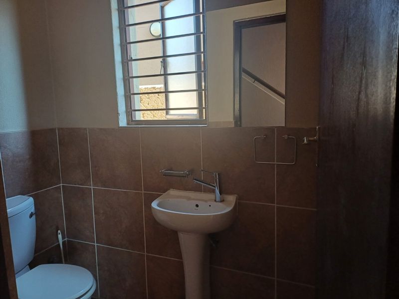 A functional guest bathroom featuring a pedestal basin, chrome mixer tap, toilet, and tiled wall finishes with a window security grill.