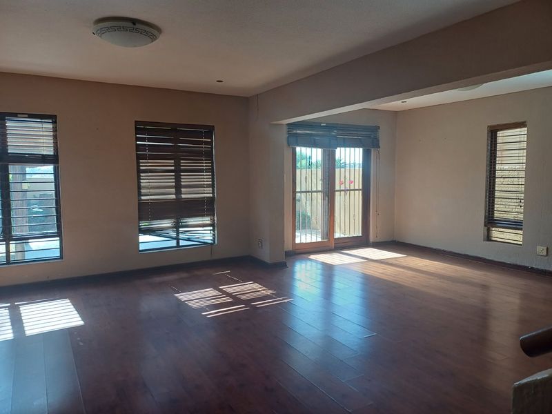 Spacious, empty living area featuring warm laminate flooring, large windows with venetian blinds, and a sliding door providing access to the exterior.