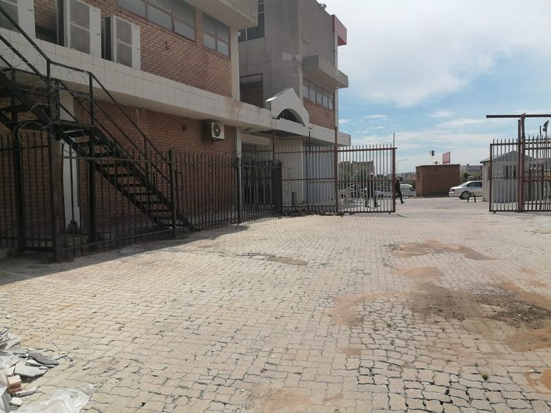 Commercial property exterior featuring a brick facade, paved driveway, metal security fencing, and an external staircase.