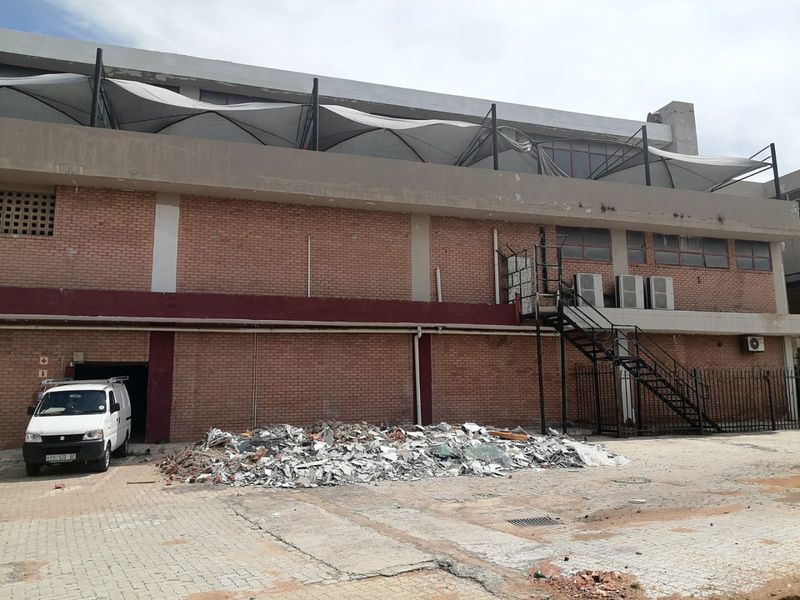 Rear exterior view of a commercial building featuring brick facade, external metal staircase, and a damaged tensile canopy structure over a paved yard.