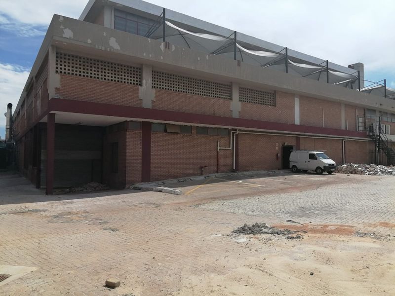 Rear exterior view of a commercial brick building featuring a roller shutter door, paved yard area, and external staircase access.