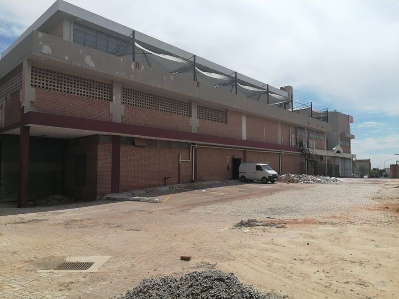 Rear exterior view of a commercial building featuring a brick facade, paved yard area, external staircase, and overhead shade sails.