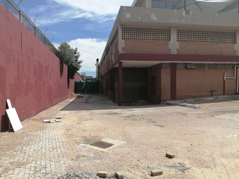 Rear exterior view of a commercial building featuring a brick facade, roller shutter door, and paved yard area with perimeter security fencing.