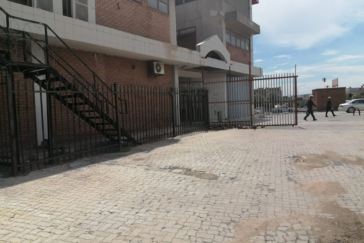 Commercial property exterior featuring a brick facade, metal security fencing with razor wire, and a paved driveway area.