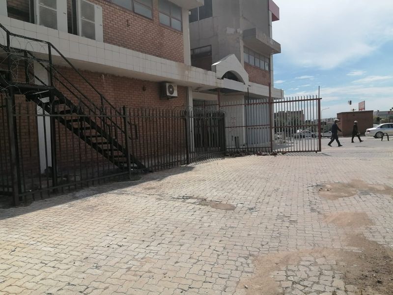Commercial property exterior featuring a brick facade, metal security fencing with razor wire, and a paved driveway area.