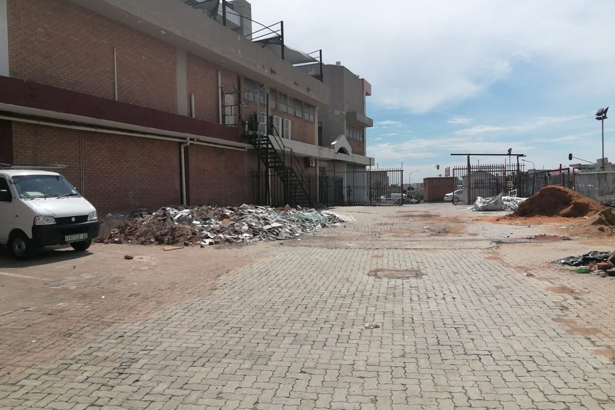 Rear exterior view of a commercial property featuring a paved yard, metal security fencing, and an external staircase, currently showing significant construction debris.
