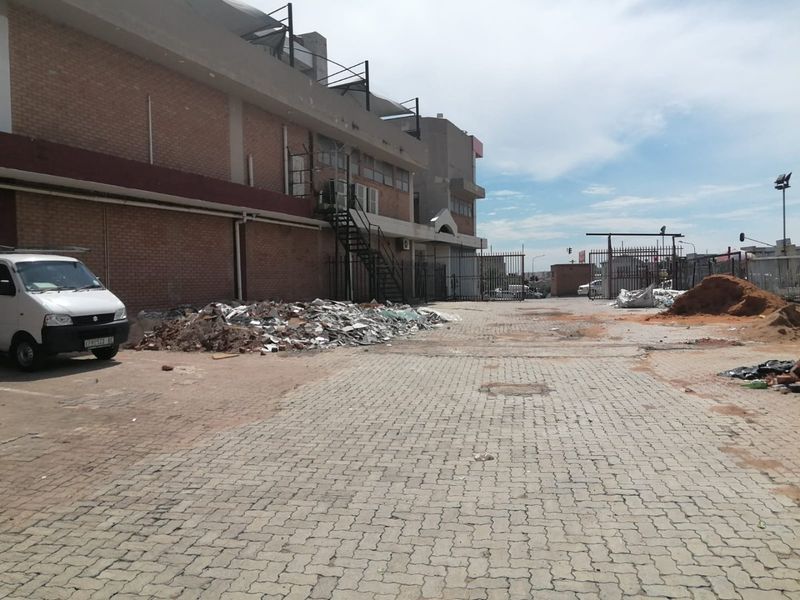 Rear exterior view of a commercial property featuring a paved yard, metal security fencing, and an external staircase, currently showing significant construction debris.
