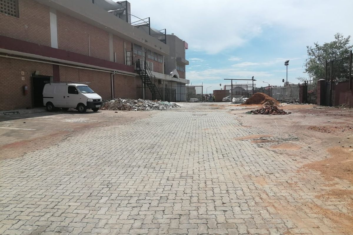 Rear exterior area of a commercial property featuring a paved driveway, brick building facade, and metal staircase access.
