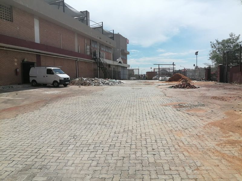 Rear exterior area of a commercial property featuring a paved driveway, brick building facade, and metal staircase access.