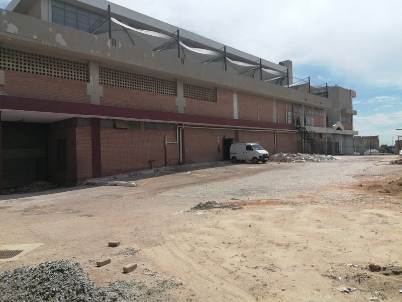 Rear exterior view of a commercial building featuring brick facade, roller shutter access, and a large paved yard area requiring maintenance.